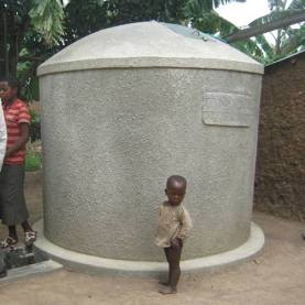 A kid stands close to a water tank. Rainwater tanks are vital in water harvest and storage